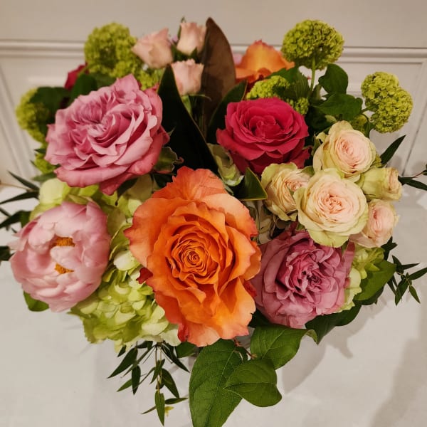 Mixed bouquet of orange, pink, and peach roses with pink peonies in a compact arrangement