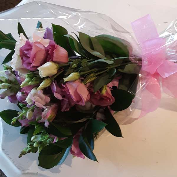 Bouquet of pink and white flowers wrapped in clear plastic with a pink bow