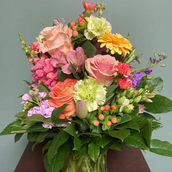 Mixed bouquet of pink, peach, yellow, and purple flowers in a glass vase
