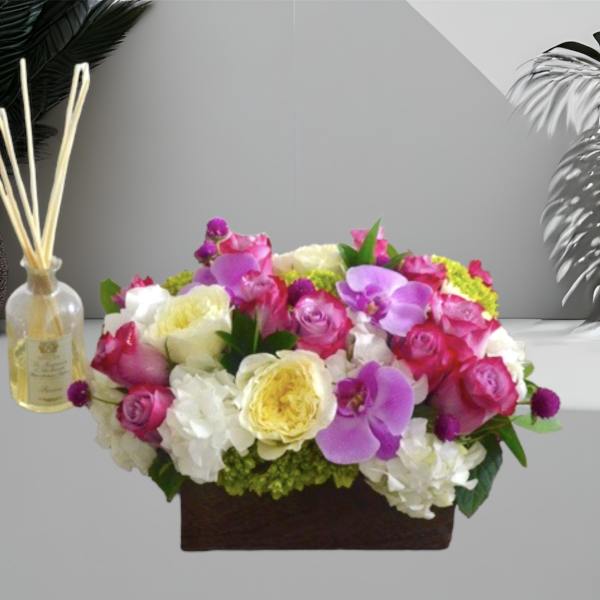 Mixed pink, white, and yellow flowers in a rectangular box with a reed diffuser