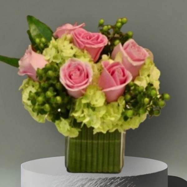 Pink roses arranged with pale green hydrangeas in a clear square vase