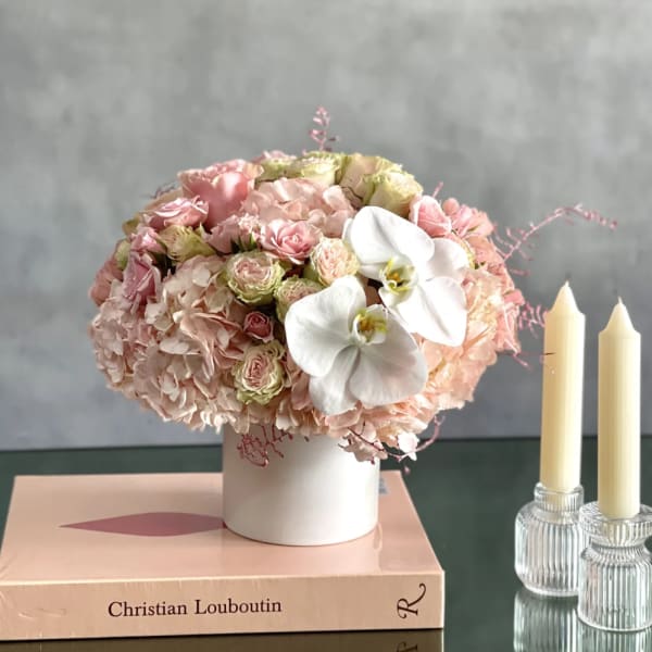 Pink floral arrangement in a white vase beside two candles