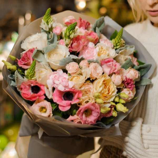 Large bouquet of pink and cream flowers wrapped in gray paper