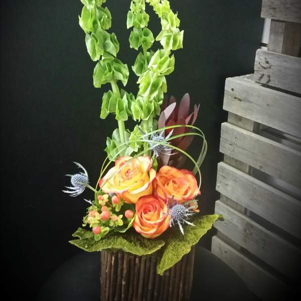 Tall floral arrangement with orange roses and green spikes in a rustic container