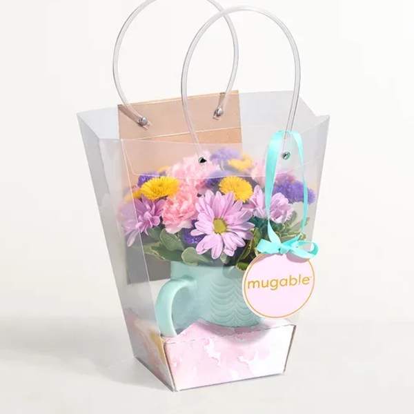 Pastel flower arrangement in a mint watering can inside a clear gift bag