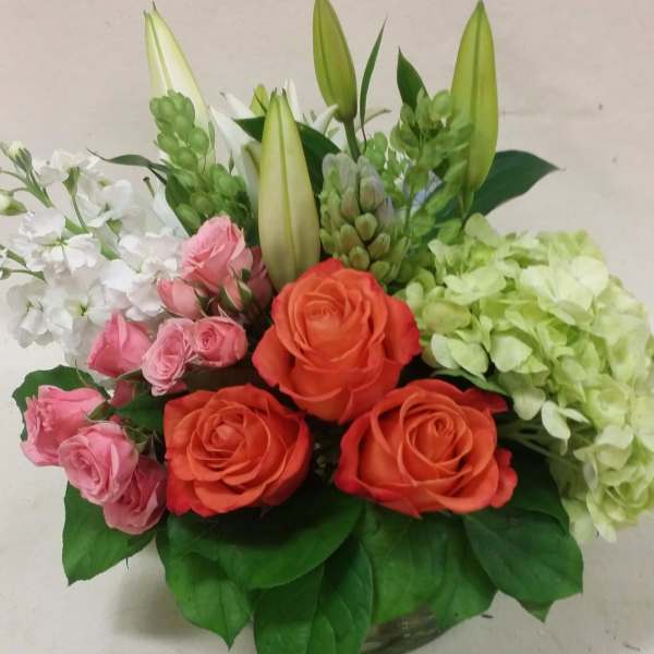Bouquet of orange and pink roses with white lilies and green hydrangeas in a vase