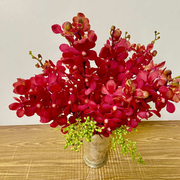 Red orchid arrangement in a clear glass vase with green berry accents