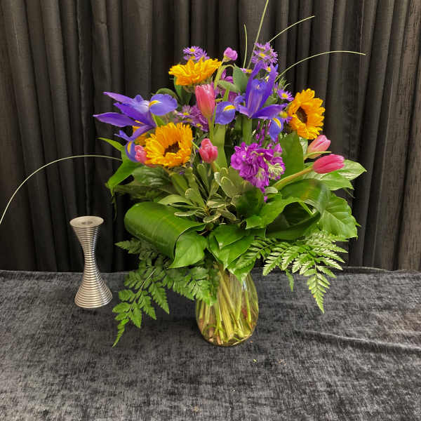 Colorful bouquet of sunflowers, irises, tulips, and purple flowers in a glass vase