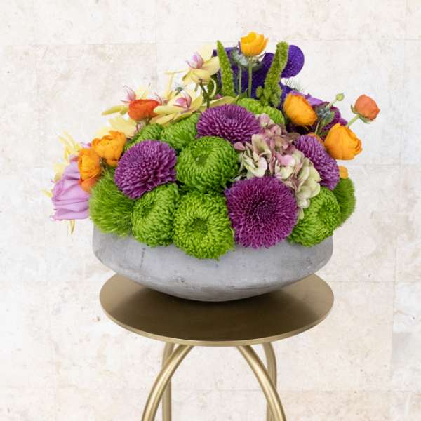 Colorful flower arrangement in a gray bowl vase on a gold stand