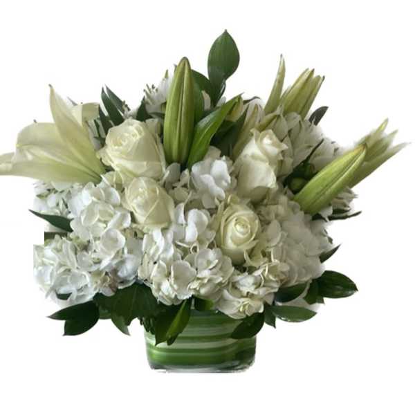 Low white arrangement of roses, lilies, and hydrangeas in a clear glass vase with green lining