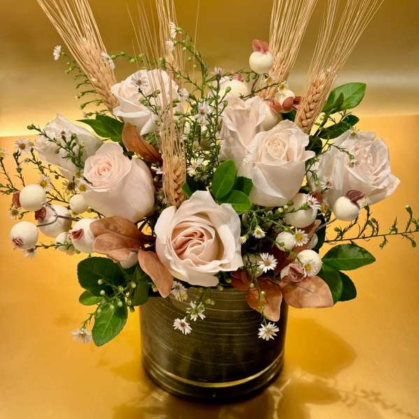 Arrangement of pale roses and wheat in a dark vase