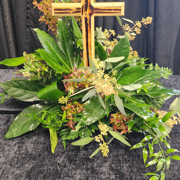 Cross-shaped floral tribute with mixed greenery and small pale blooms