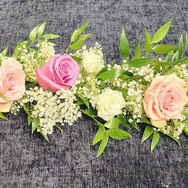 Long floral garland with pink and cream roses on a dark surface