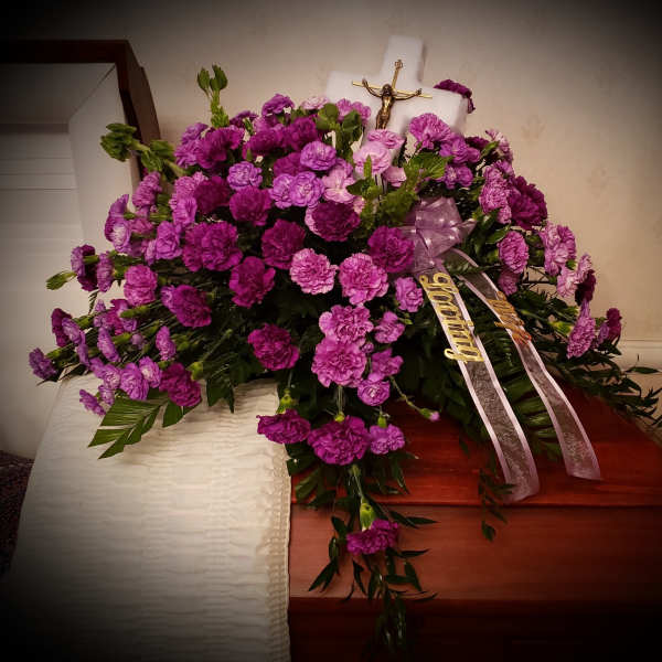Purple carnation funeral spray with ribbons on a casket