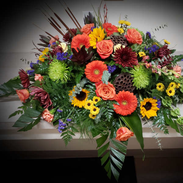 Large colorful floral casket spray with roses, gerbera daisies, and sunflowers
