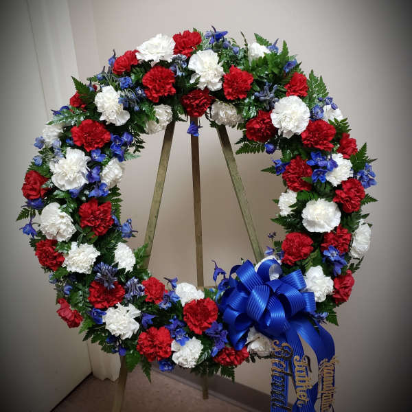 Red, white, and blue floral wreath on a stand with a ribbon bow