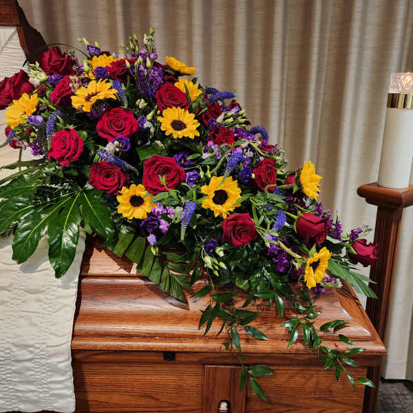 Casket spray with red roses, sunflowers, and purple flowers