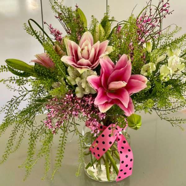 Pink lilies and mixed blooms in a glass vase with a polka-dot ribbon