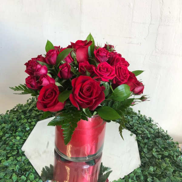 Round arrangement of red roses in a glass cylinder vase on a mirrored base