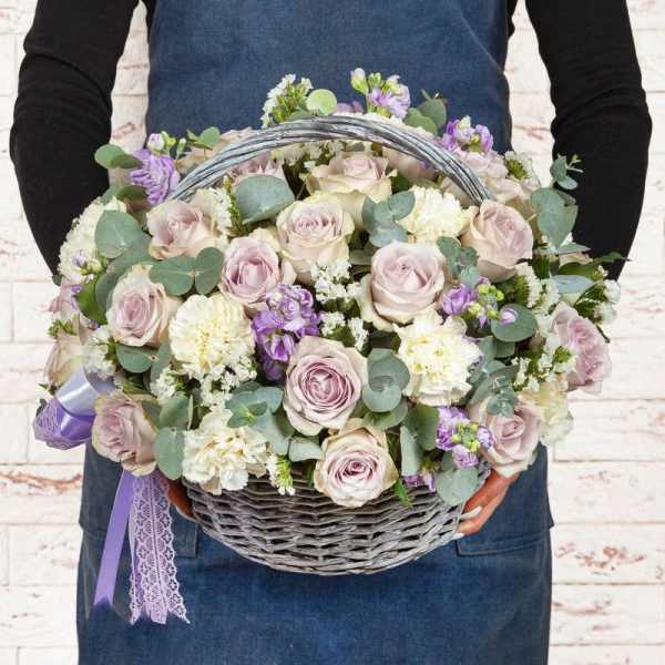 Basket of pale roses, white carnations, and purple flowers with ribbon