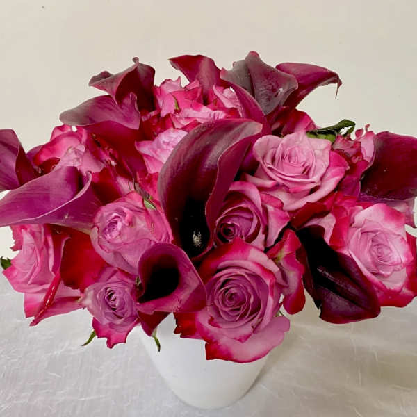 Pink roses and dark magenta calla lilies in a white vase