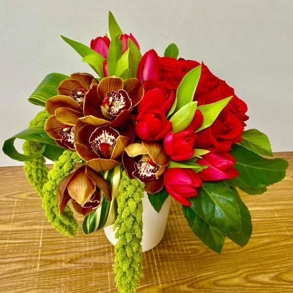Bouquet of red roses, red tulips, and orchids in a white vase