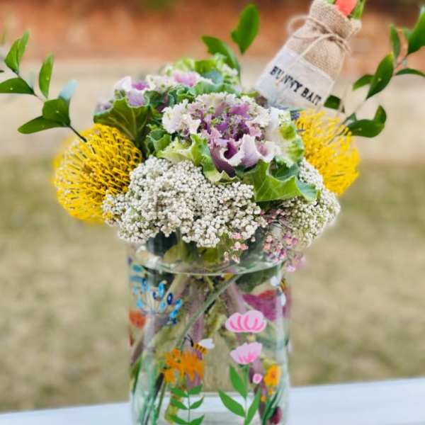 Mixed flower bouquet in a clear glass jar with a small wrapped carrot bundle