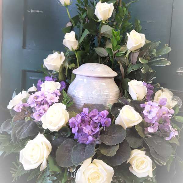 White roses and purple flowers arranged in a tall urn centerpiece