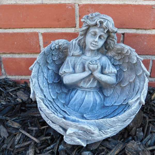 Gray angel statue holding a rose in front of a brick wall