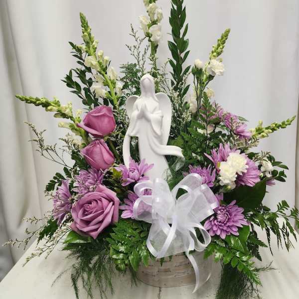 Purple and white floral arrangement with an angel figurine in a basket