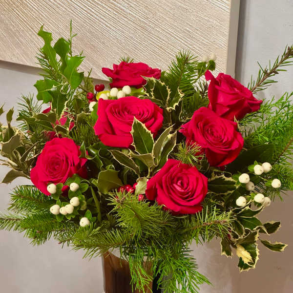 Red roses arranged in a glass vase with evergreen and white berries