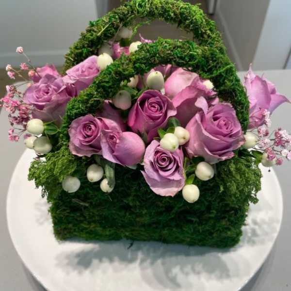 Basket arrangement of lavender roses with white berries and moss handles