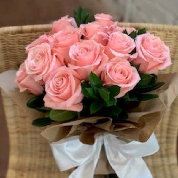 Bouquet of pink roses wrapped with brown paper and a white ribbon
