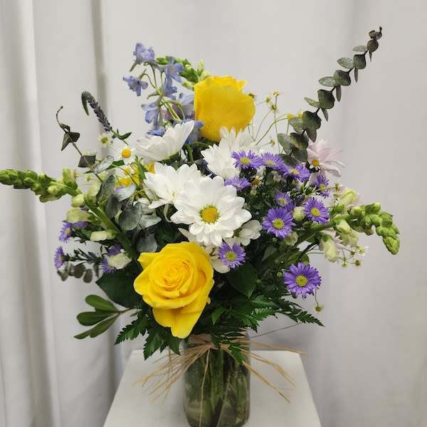 Bouquet of yellow roses, white daisies, and purple asters in a glass vase