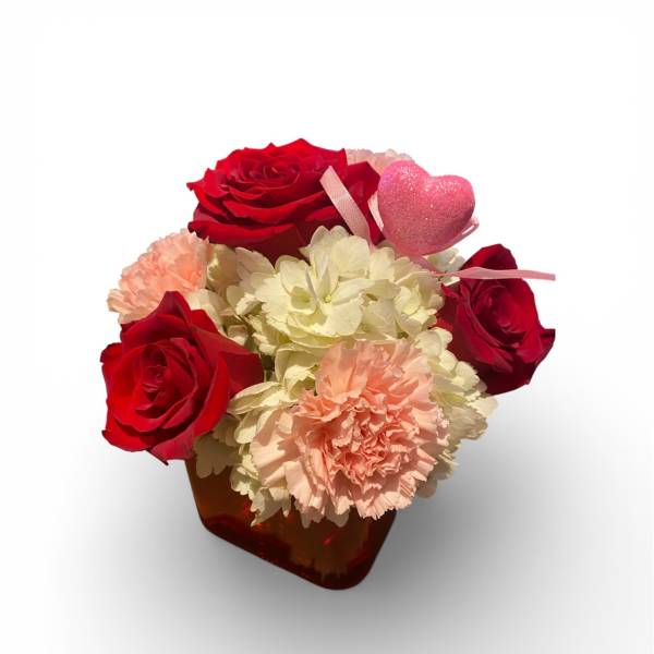 Red roses and pale carnations in a small vase with a pink heart pick