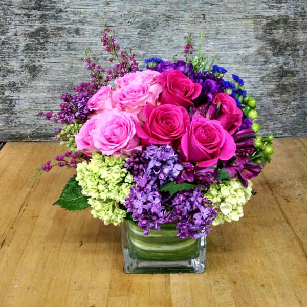 Pink and purple rose arrangement in a square glass vase