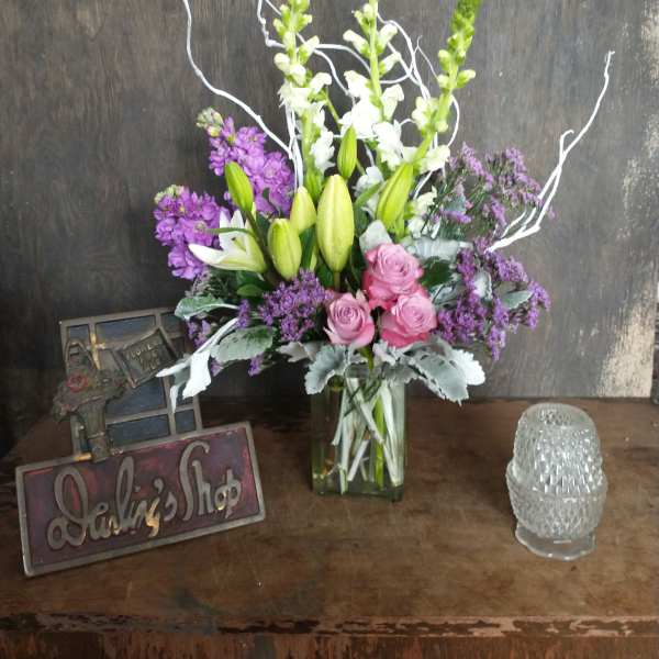 Tall bouquet of lilies, roses, and purple flowers in a glass vase