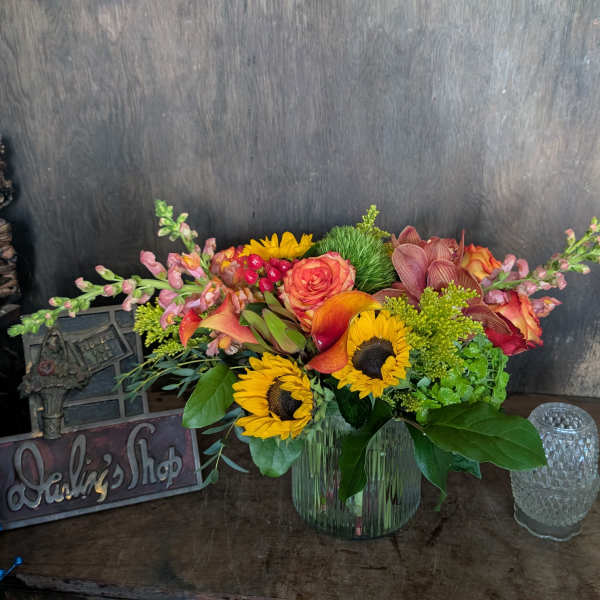 Mixed bouquet of sunflowers, roses, and orchids in a glass vase
