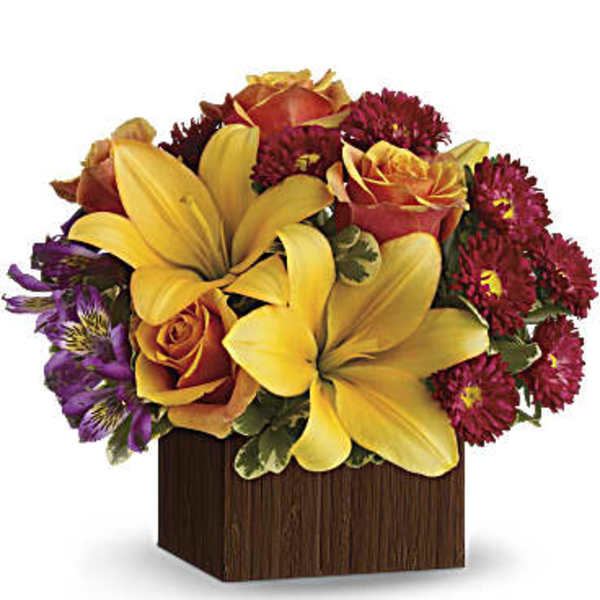 Bouquet of yellow lilies, orange roses, and red daisies in a wooden cube vase