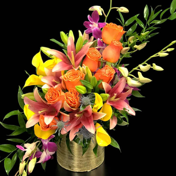 Orange roses with pink lilies and yellow calla lilies in a gold vase