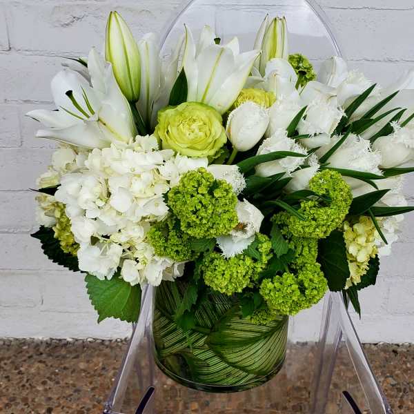 White lilies and green-white blooms arranged in a glass vase