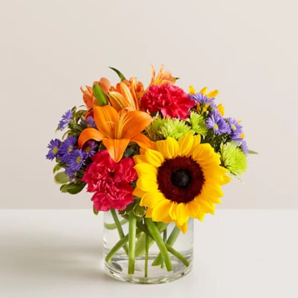 Colorful mixed bouquet in a clear glass vase with a sunflower and lilies