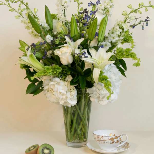 White lilies and roses in a glass vase with kiwi and a teacup