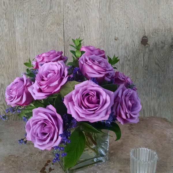 Lavender rose bouquet in a clear square vase with purple filler flowers