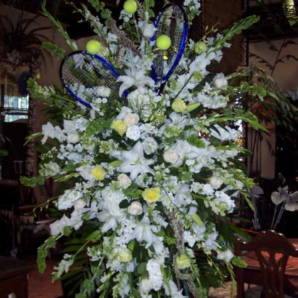 Large white floral standing arrangement with blue tennis rackets and tennis balls