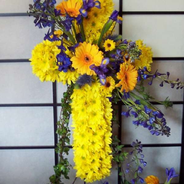 Cross-shaped floral arrangement with yellow and orange daisies and blue flowers