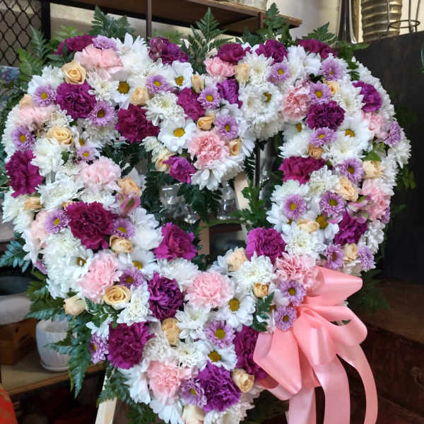 Heart-shaped floral wreath with pink ribbon and mixed pink, white, and purple flowers