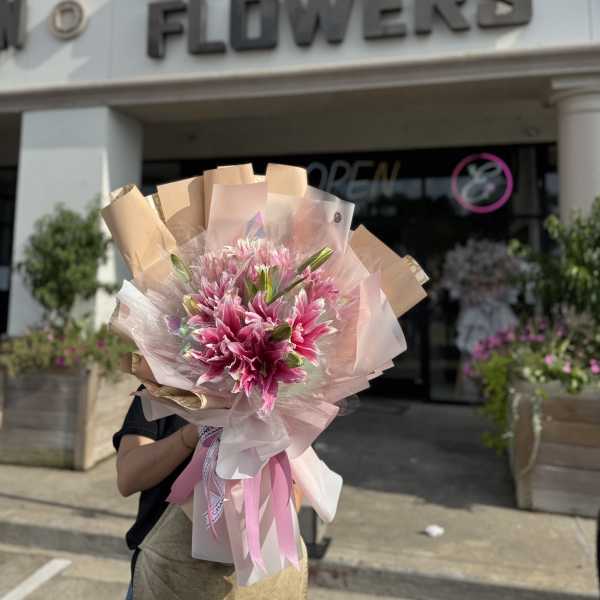 Pink lily bouquet wrapped in blush and tan paper with ribbon