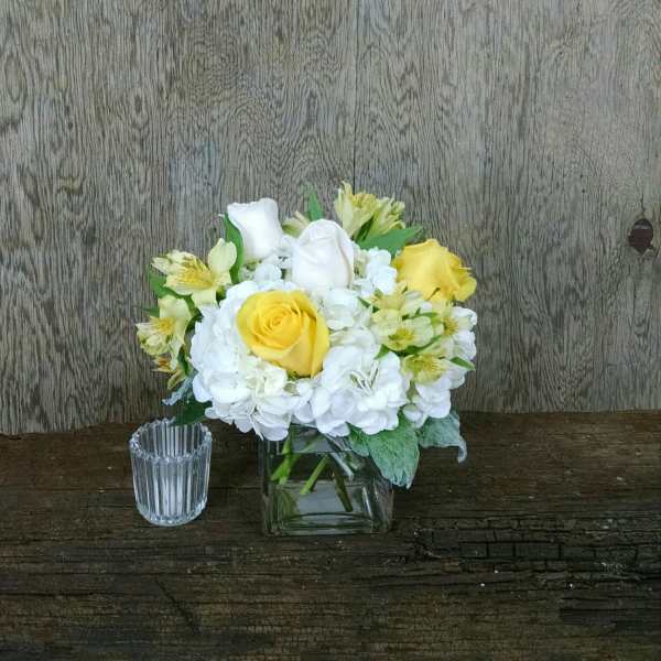 Yellow and white roses in a square glass vase with white hydrangeas
