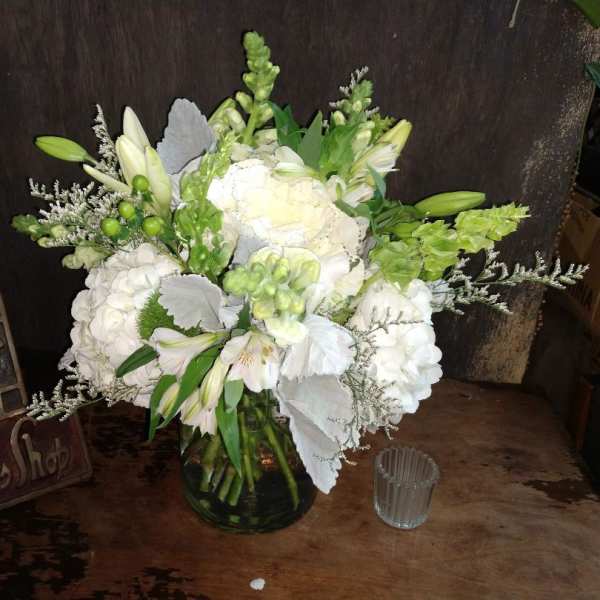 White floral arrangement in a glass vase with green accents